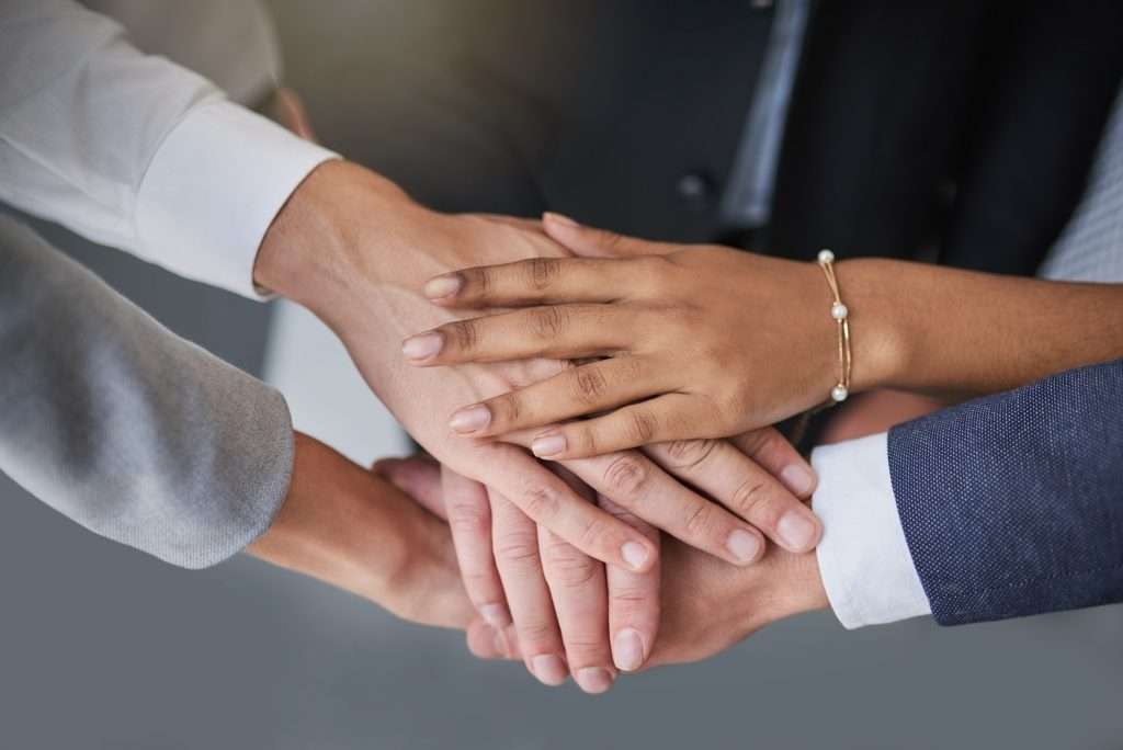 Cropped shot of a group of colleagues joining hands in solidarity in a modern office